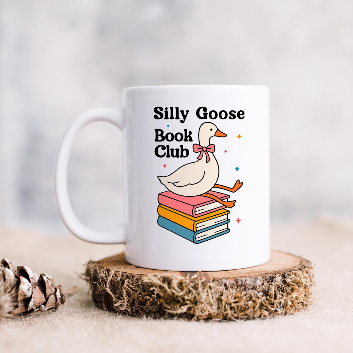 A white mug with a colorful illustration of a duck sitting on a stack of books, along with the text "Silly Goose Book Club".