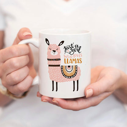 A person is holding a white mug with a pink llama design on it.