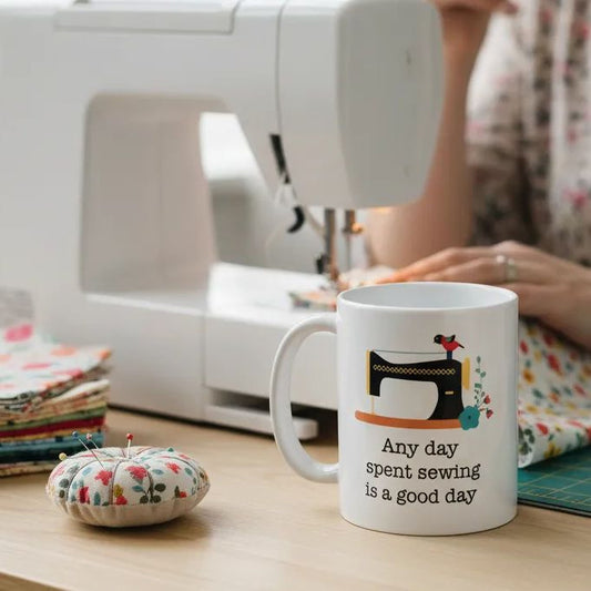 A sewing machine, a mug with a sewing-themed design, and a stack of fabric are visible in the image.