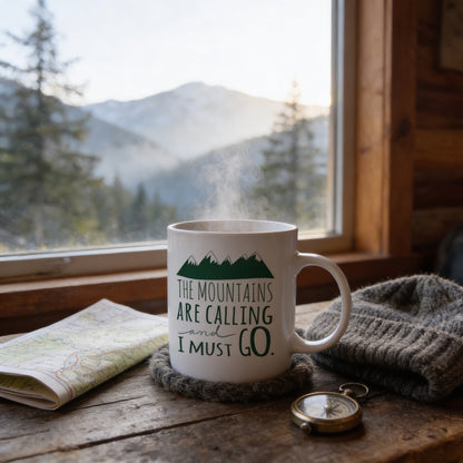 A mug with the text "The mountains are calling and I must go" sits on a wooden table, with a map and a compass nearby. The mug is placed near a window overlooking a mountainous landscape.