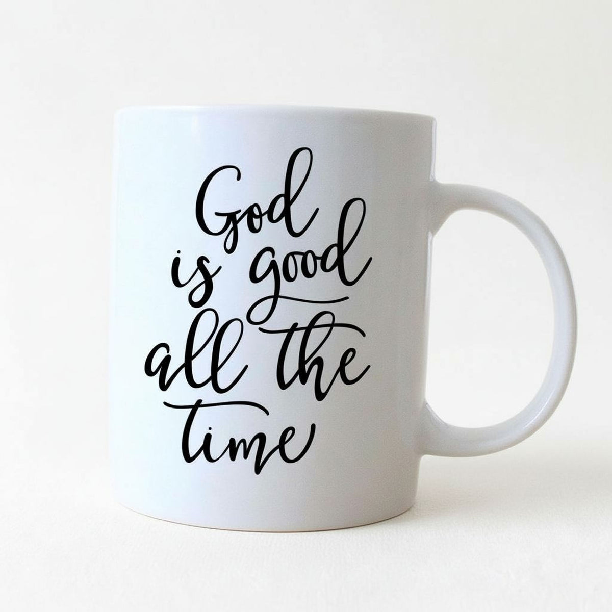 A white ceramic mug with black text that reads "God is good all the time".