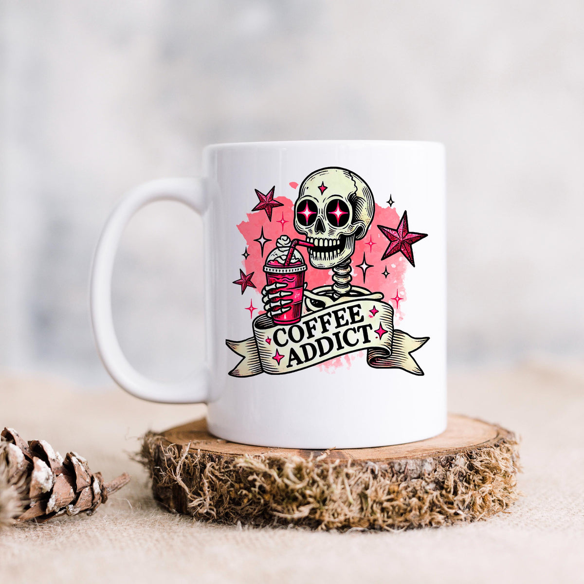 A white mug with a skull design and the text "COFFEE ADDICT" printed on it, along with a star and a ribbon.