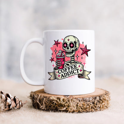 A white mug with a skull design and the text "COFFEE ADDICT" printed on it, along with a star and a ribbon.