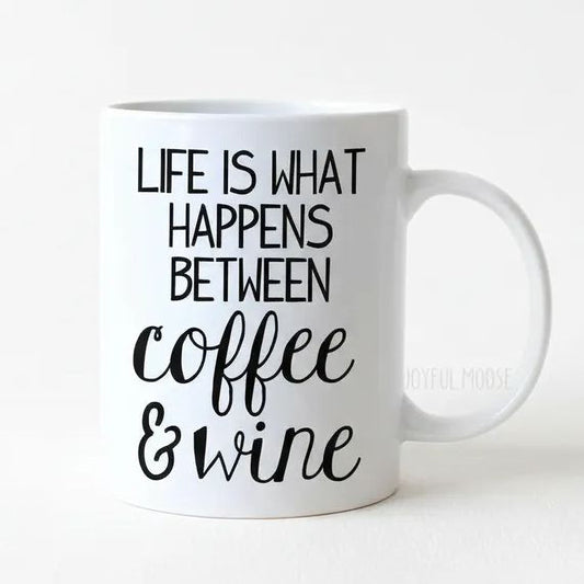 A white ceramic mug with black text that reads "LIFE IS WHAT HAPPENS BETWEEN COFFEE & WINE".