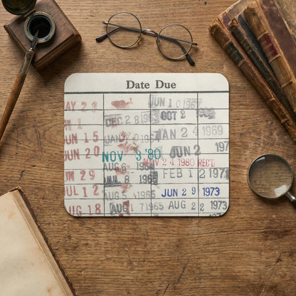 a wooden desk with various items, including a date due card, glasses, a magnifying glass, and some books.