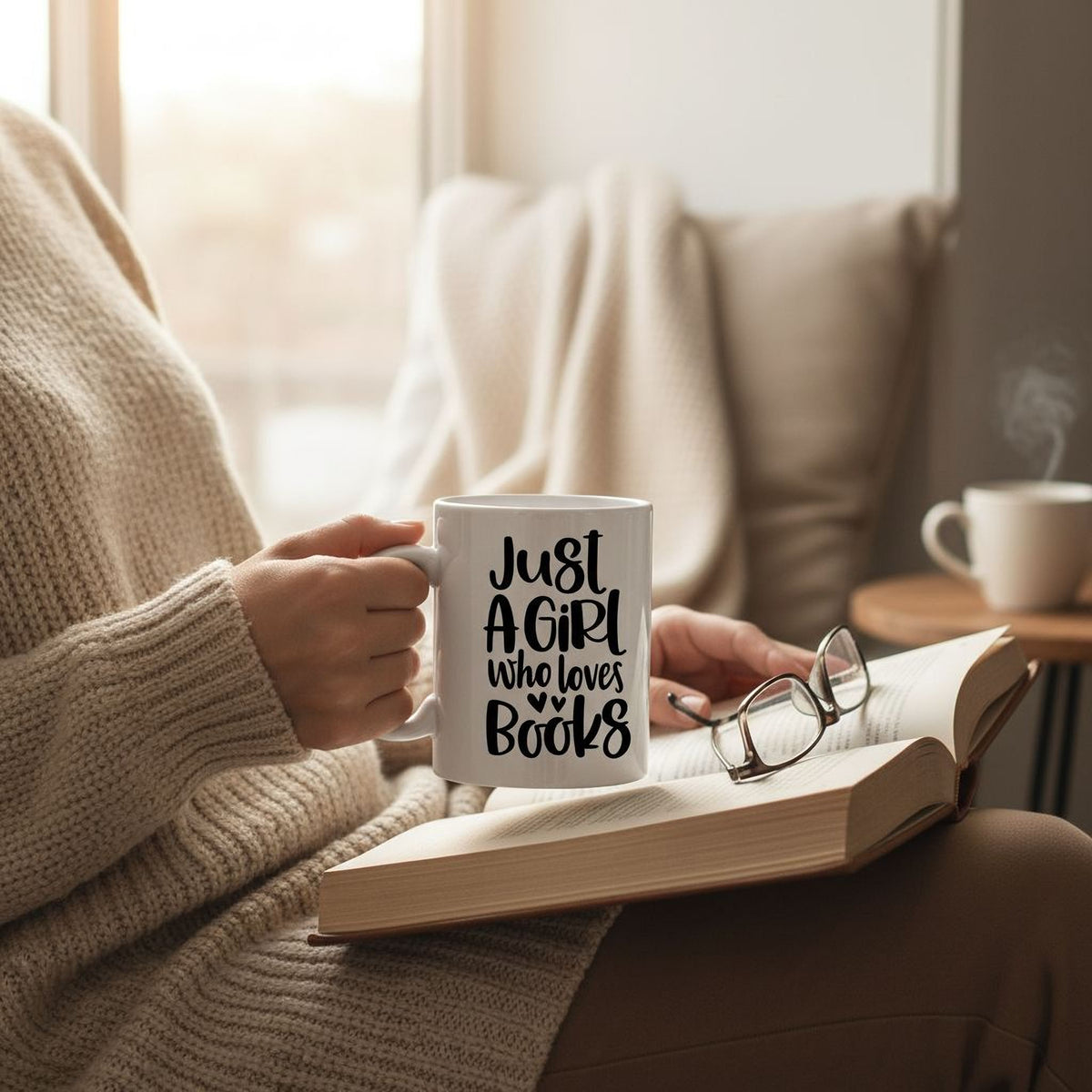 A person is sitting in a chair, holding a mug with the text "Just a girl who loves books" while reading a book.