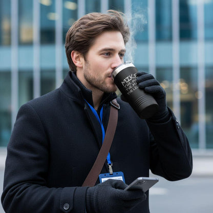 A man in a black coat is holding a black coffee mug and looking at his phone, with steam rising from the mug.
