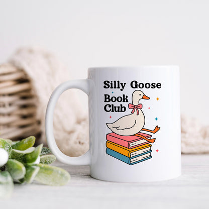 A white mug with a colorful illustration of a duck sitting on a stack of books, along with the text "Silly Goose Book Club".