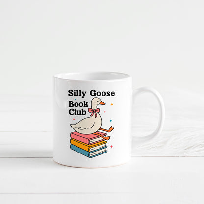A white mug with a colorful illustration of a duck sitting on a stack of books, along with the text "Silly Goose Book Club".