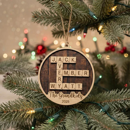 A wooden ornament with letters spelling out "JACK VEMBER WYATT" hangs on a Christmas tree, surrounded by twinkling lights and greenery.