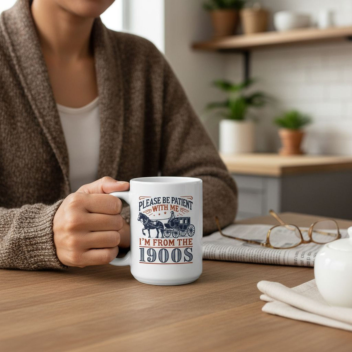 A person is sitting at a table, holding a mug with a humorous text printed on it.