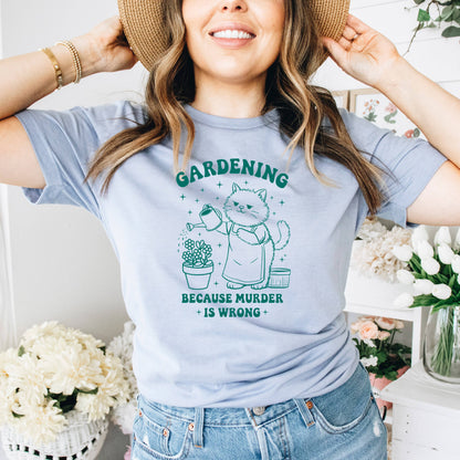 A woman wearing a gray t-shirt with a graphic design of a cat watering plants and the text "Gardening because murder is wrong".