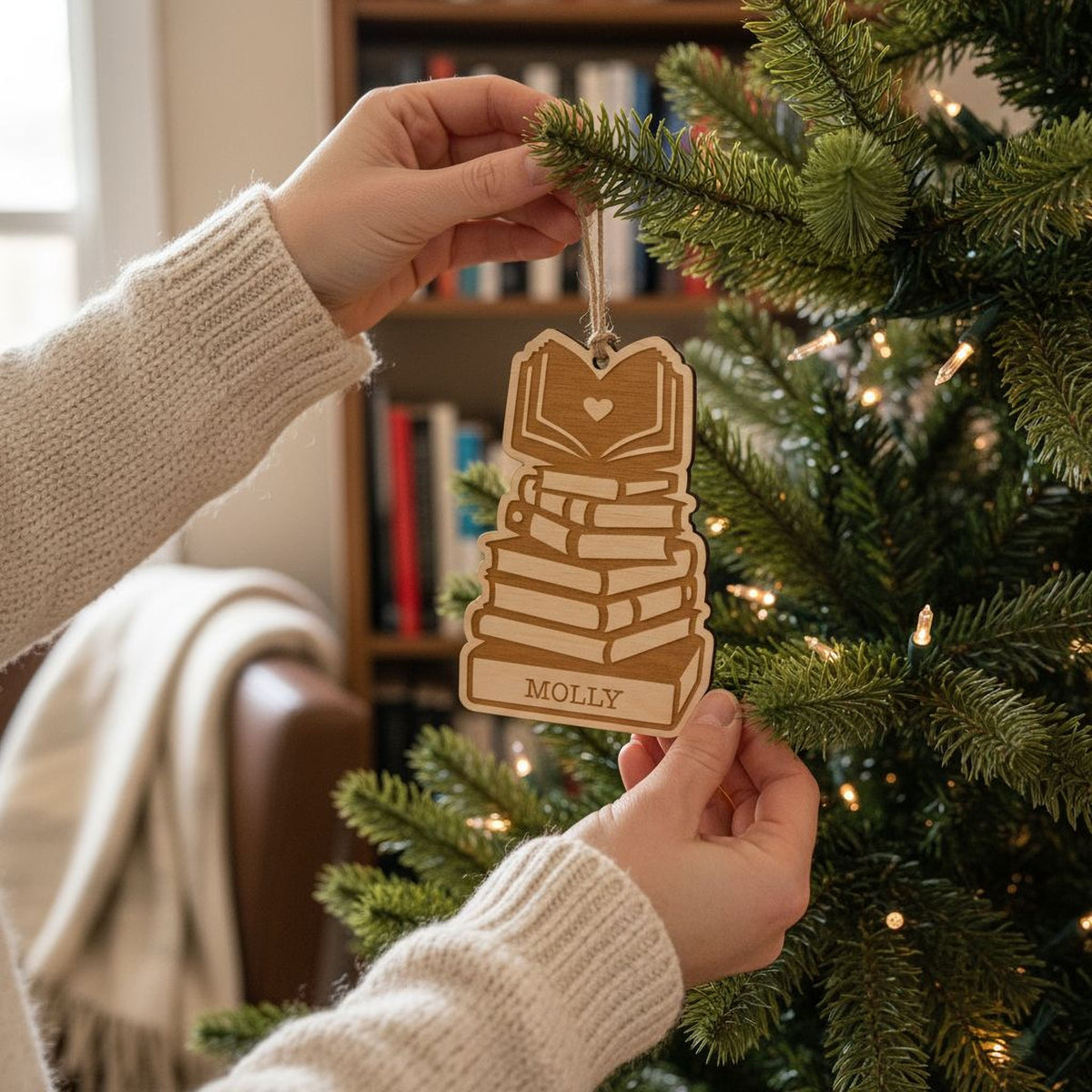 A person's hands holding a wooden ornament with a stack of books on top, hanging from a Christmas tree.