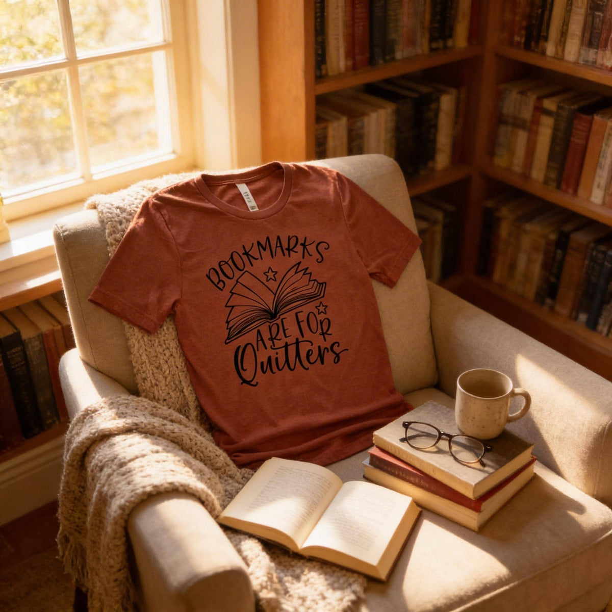 A cozy scene with a red t-shirt on a beige armchair, a stack of books, a mug, and a pair of glasses, all bathed in soft light from a nearby window.