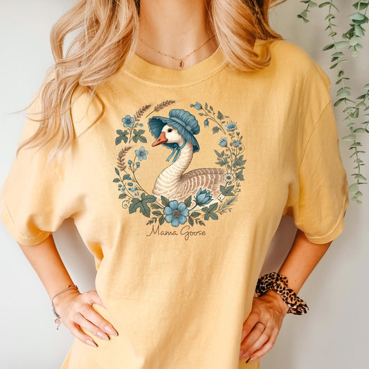 May include: A yellow short-sleeved t-shirt with a floral design featuring a goose wearing a blue bonnet. The text 'Mama Goose' is printed below the design.