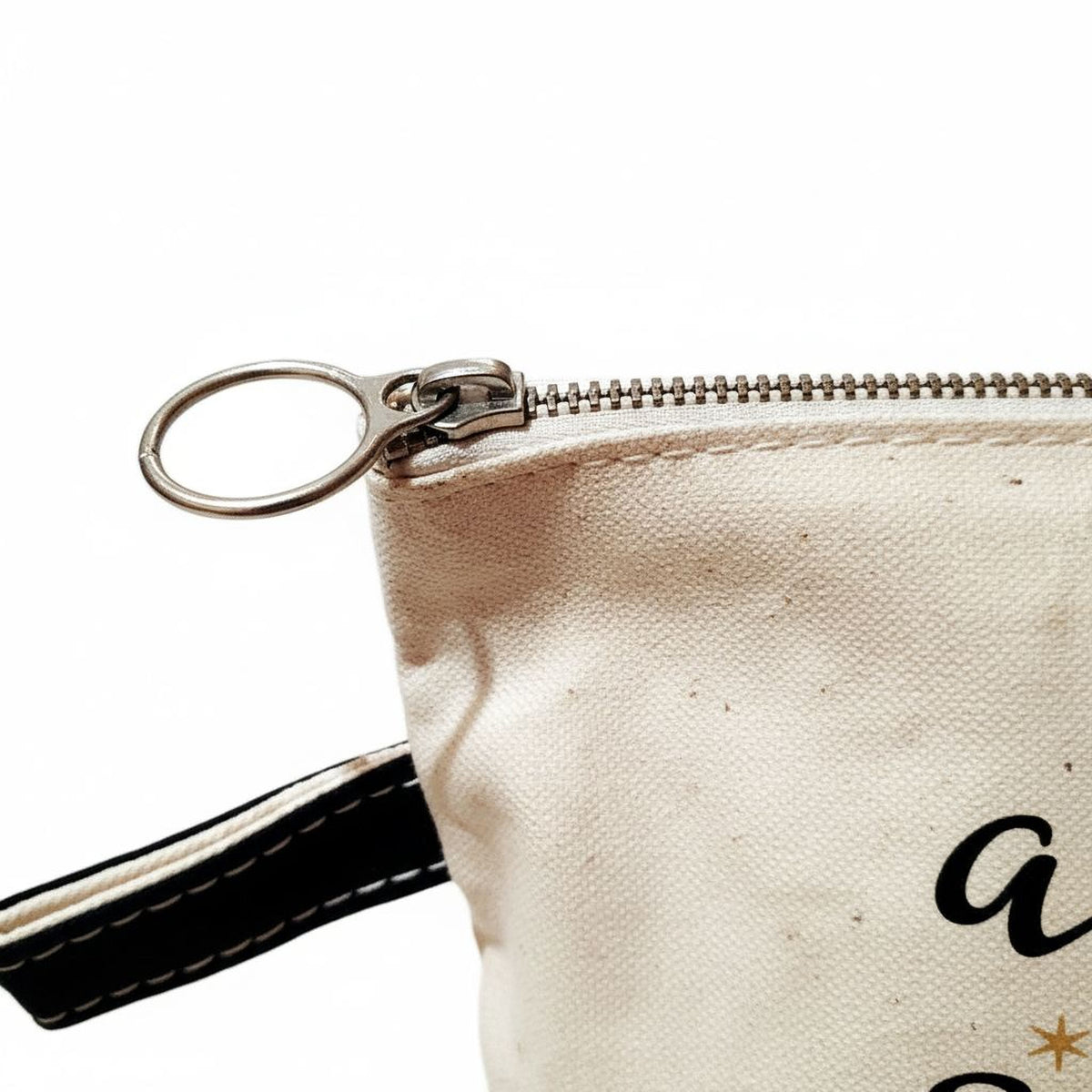 A close-up view of a zipper on a bag or pouch, with a black strap visible on the left side.