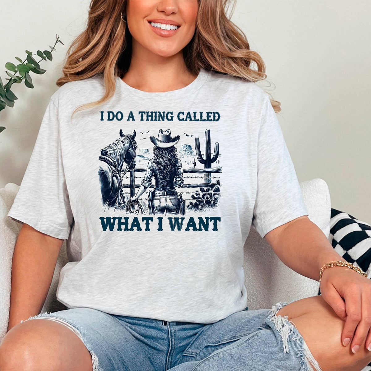 A woman wearing a white t-shirt with a graphic design of a cowboy and a cactus, along with the text "I DO A THING CALLED WHAT I WANT".