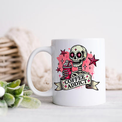 A white mug with a skull design and the text "COFFEE ADDICT" printed on it, along with a star and a ribbon.
