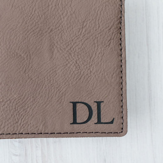 A close-up view of a brown leather wallet or card with the initials "DL" printed on it.
