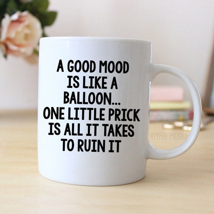 A white ceramic mug with black text printed on it, sitting on a wooden surface.