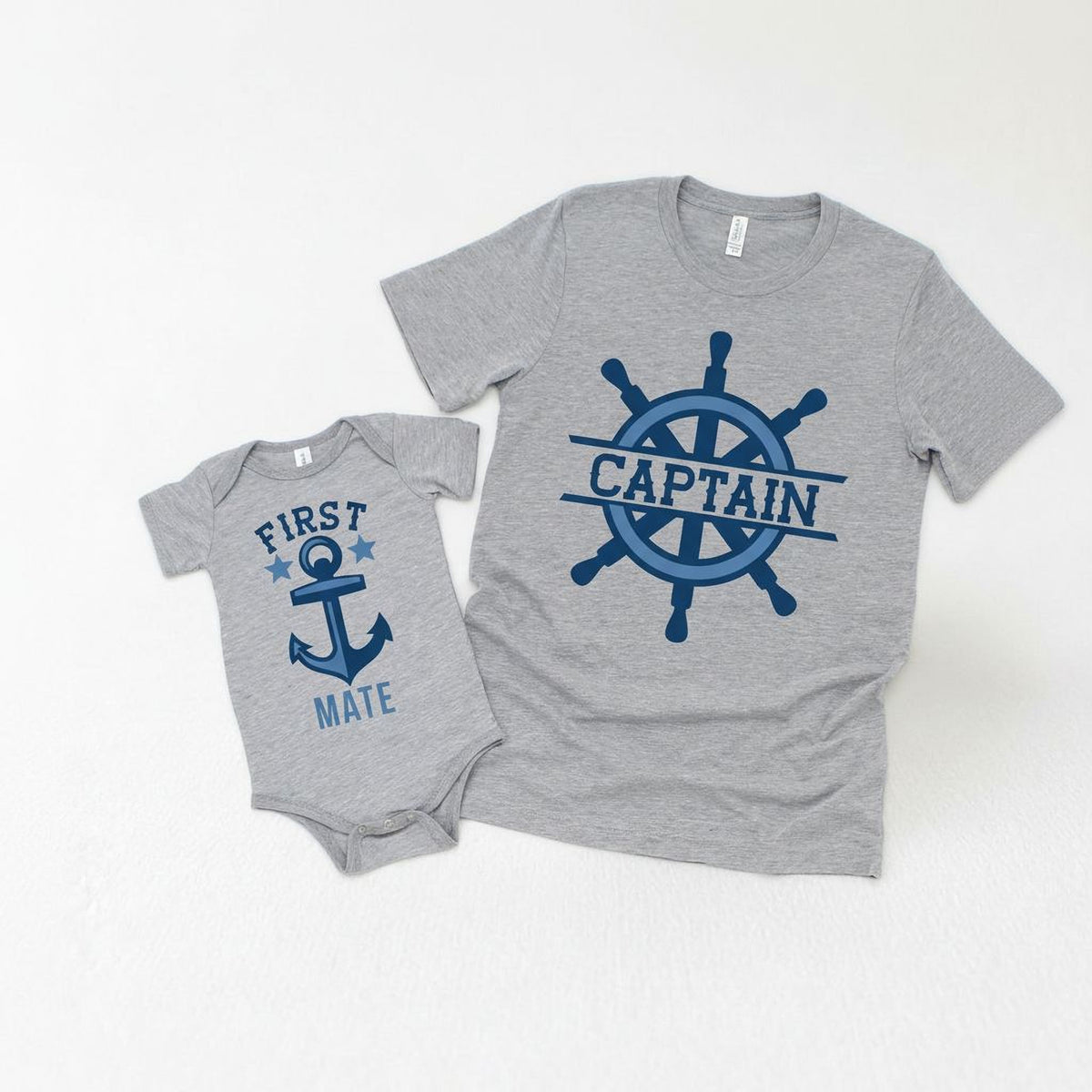 Two gray t-shirts with blue designs, one with the text "FIRST MATE" and the other with the text "CAPTAIN" and a blue anchor and ship's wheel design.
