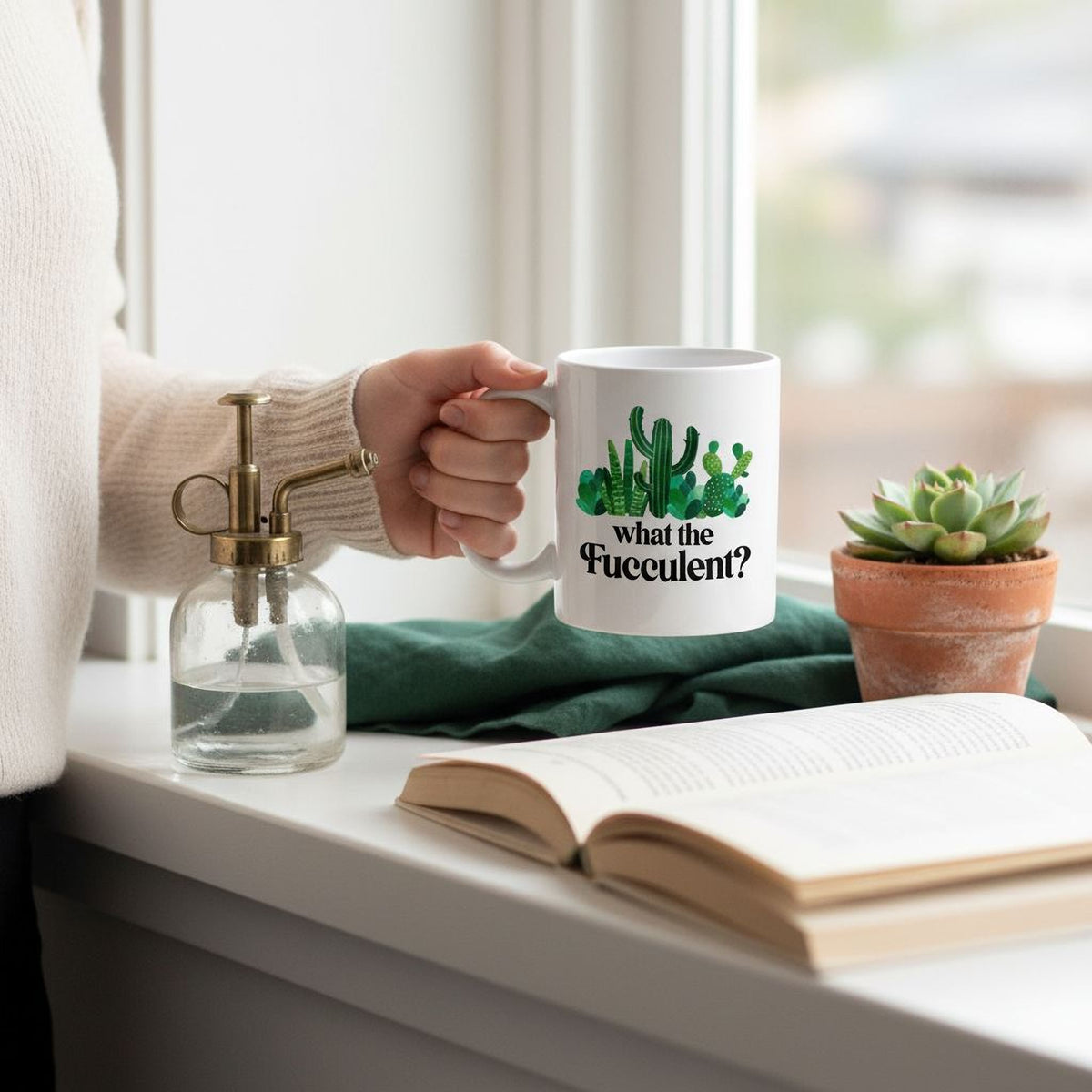A person's hand holding a mug with a graphic of cacti and the text "what the Fuzzy?"
