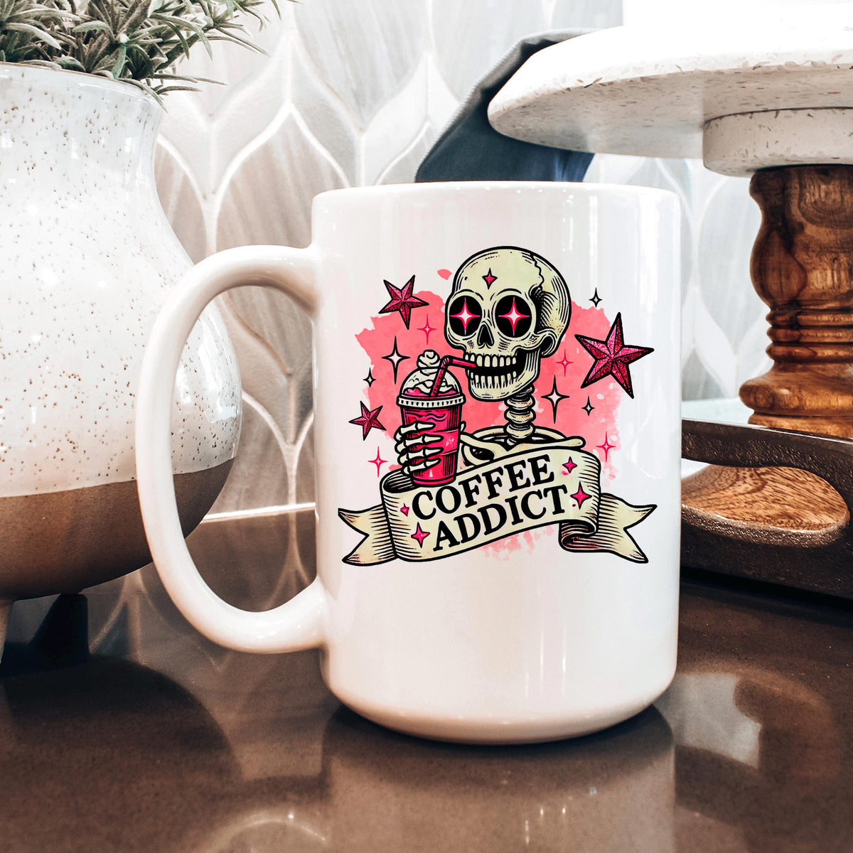 A white coffee mug with a skull design and the text "COFFEE ADDICT" printed on it, sitting on a table.