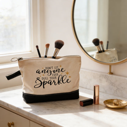 A makeup bag with a motivational quote on it, placed on a bathroom counter next to a mirror and some makeup brushes.