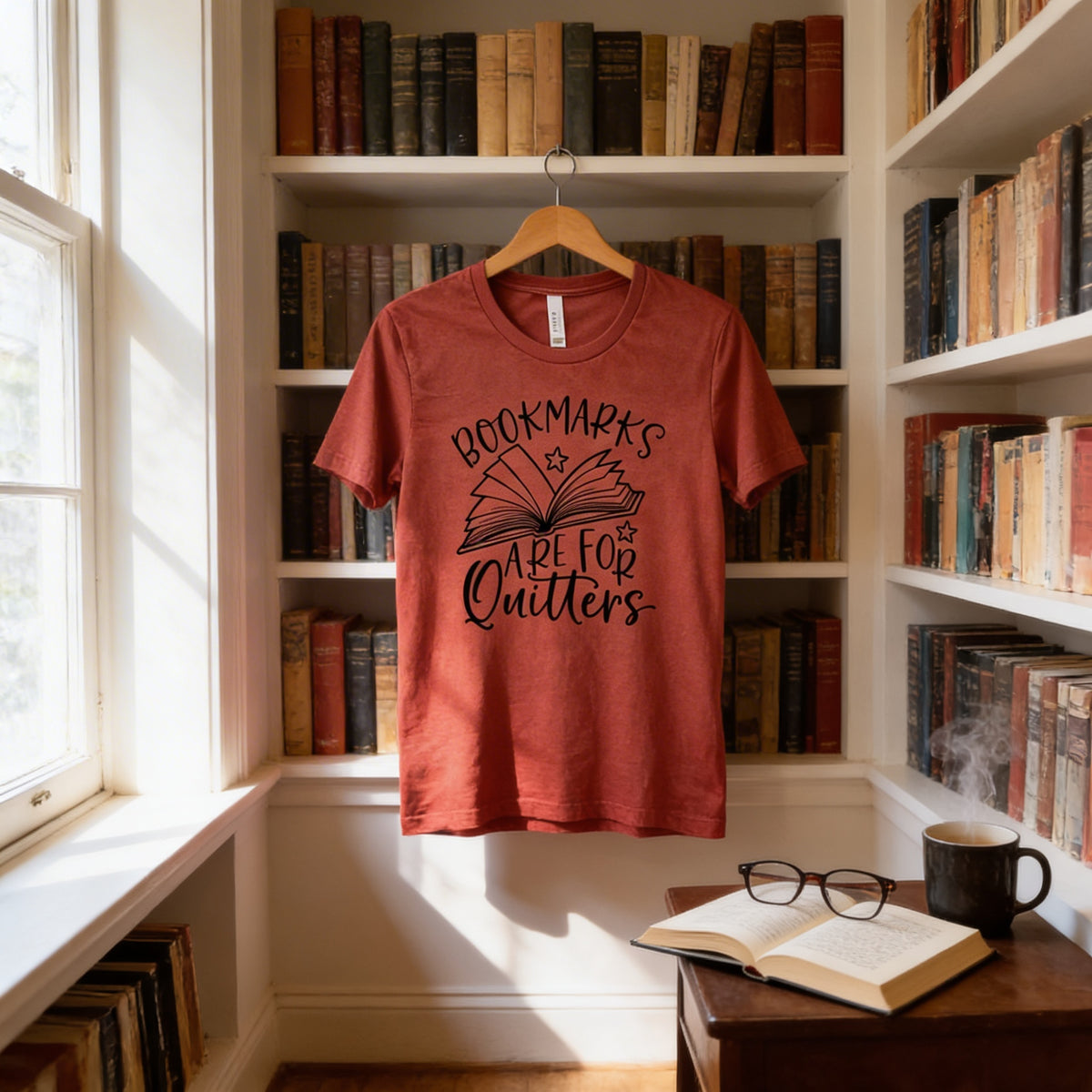 A red t-shirt with the text "BOOKMARKS ARE FOR QUITTERS" is hanging on a wooden hanger in a room filled with bookshelves.