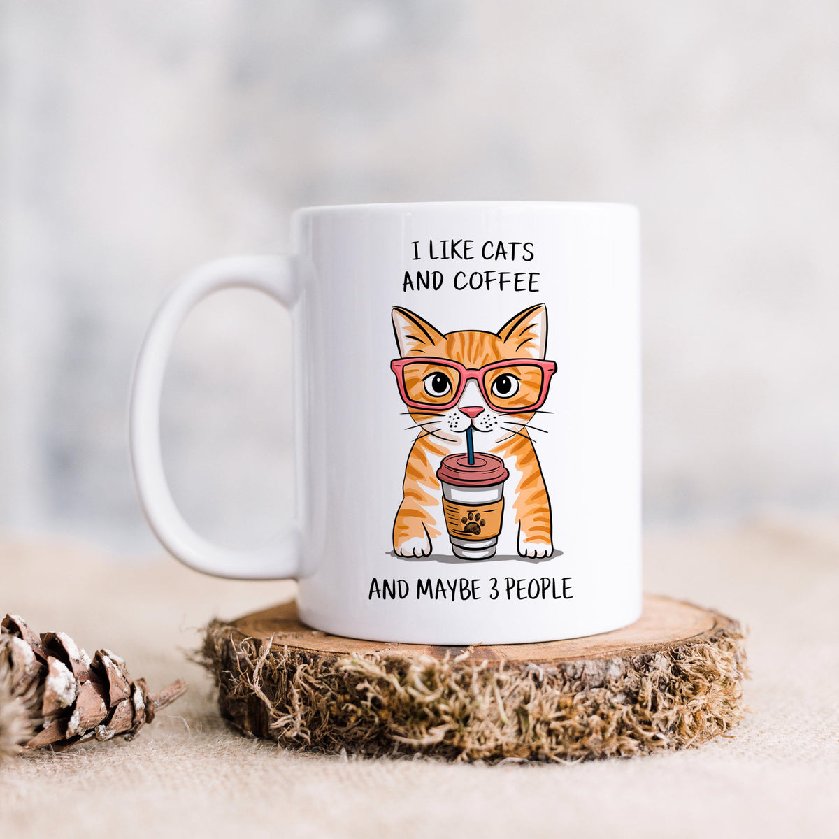 A white mug with an illustration of a cat wearing glasses and holding a coffee cup, accompanied by the text "I LIKE CATS AND COFFEE AND MAYBE 3 PEOPLE".