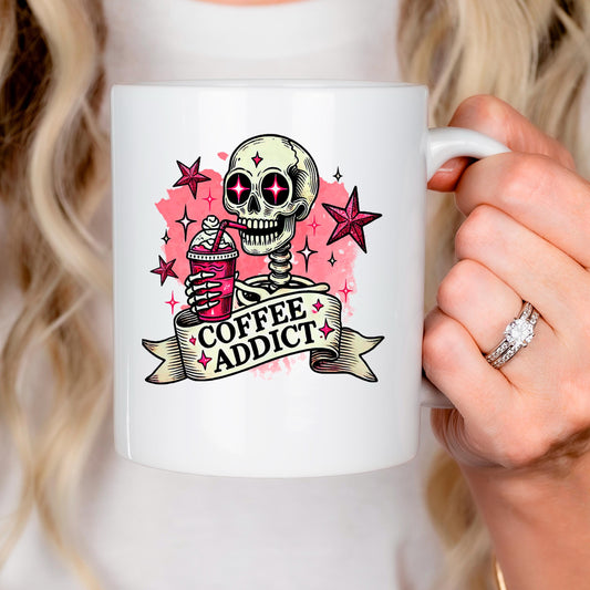 A person is holding a white mug with a skull design and the text "COFFEE ADDICT" printed on it.