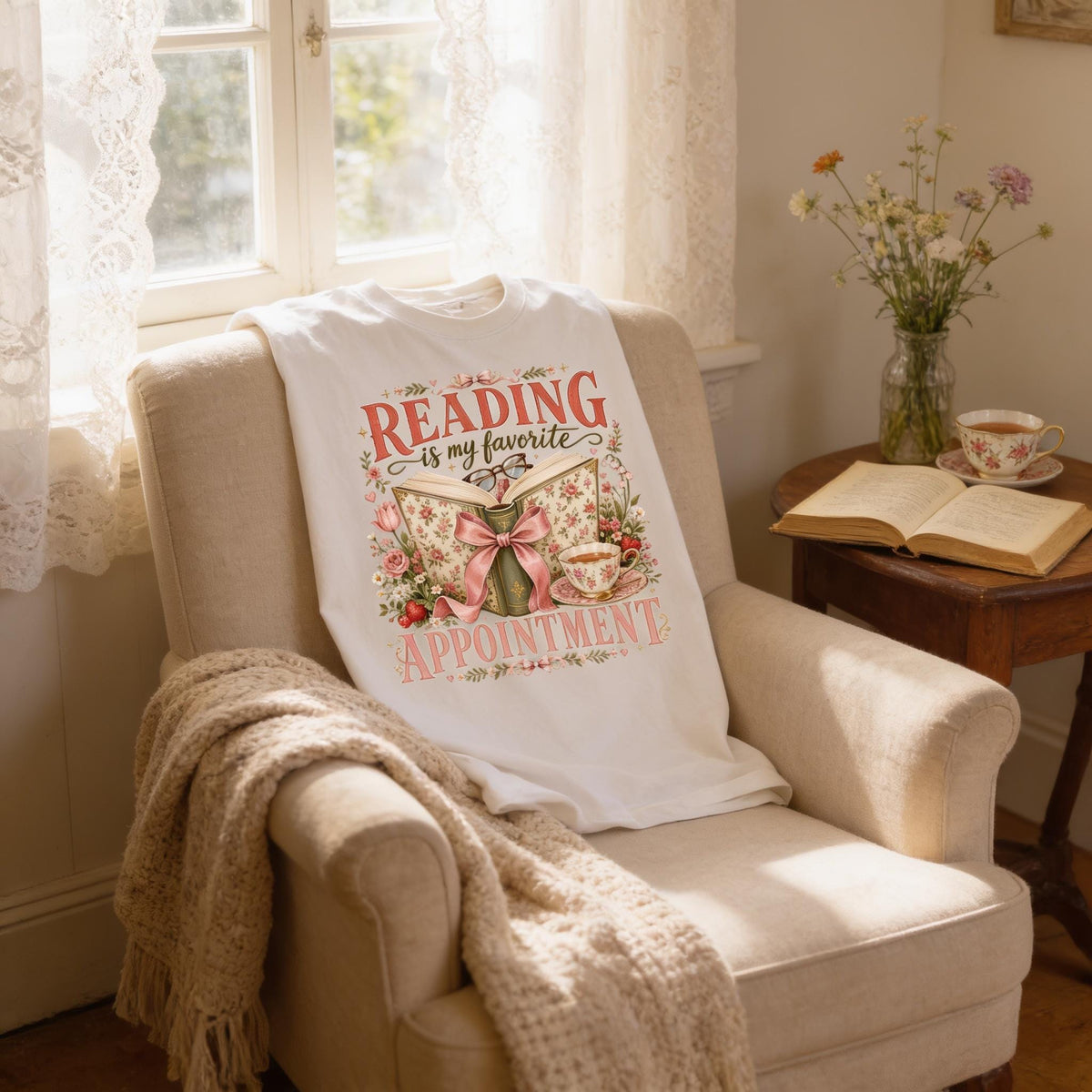 A cozy reading nook in a room with a beige armchair, a white t-shirt with a floral design, and a vase of flowers on a small table.