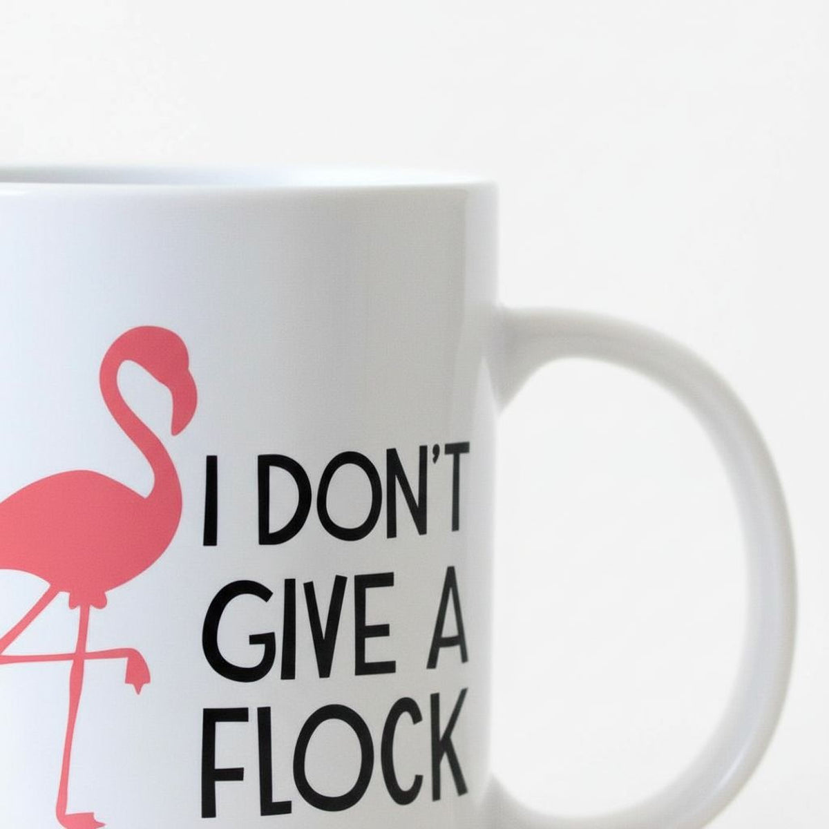 A white mug with a pink flamingo design and the text "I DON'T GIVE A FLOCK" printed on it.