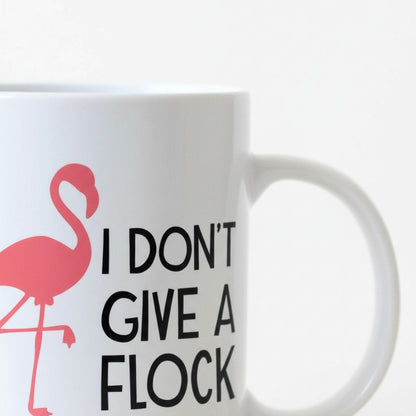 A white mug with a pink flamingo design and the text "I DON'T GIVE A FLOCK" printed on it.