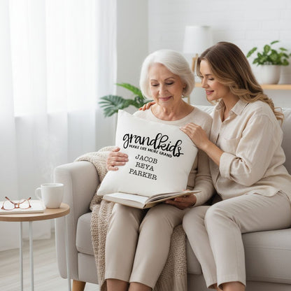 Two women sitting on a couch, one older and one younger, are looking at a book together. The older woman is holding a pillow with the text "Grandkids" written on it.