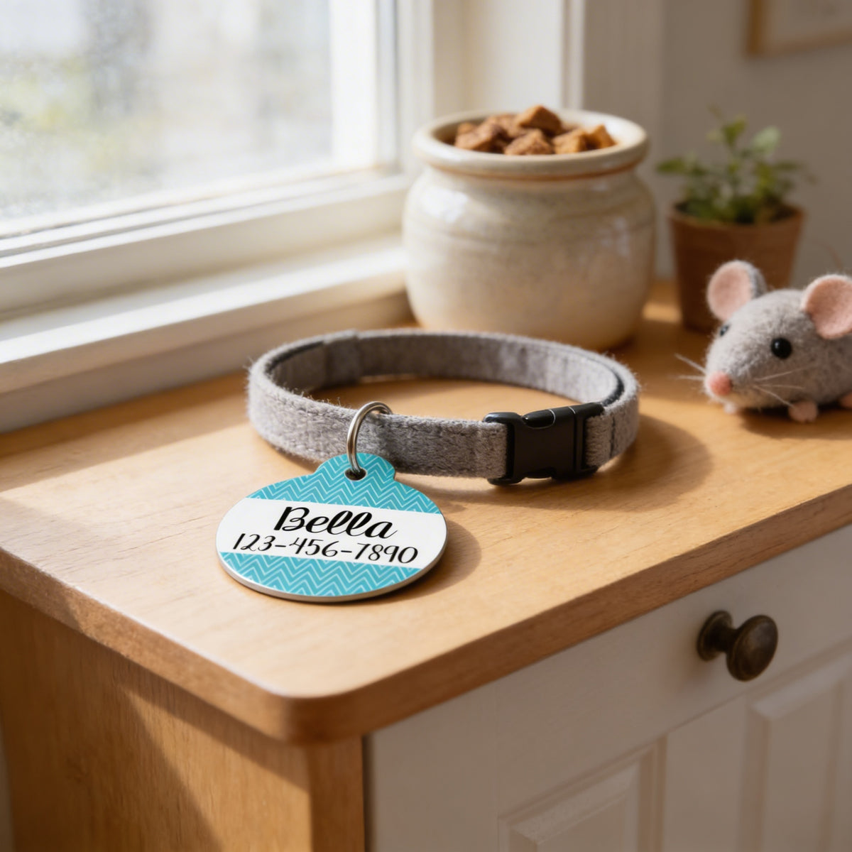 A gray collar with a name tag, a small stuffed mouse, and a ceramic dish with cat food are arranged on a wooden surface.