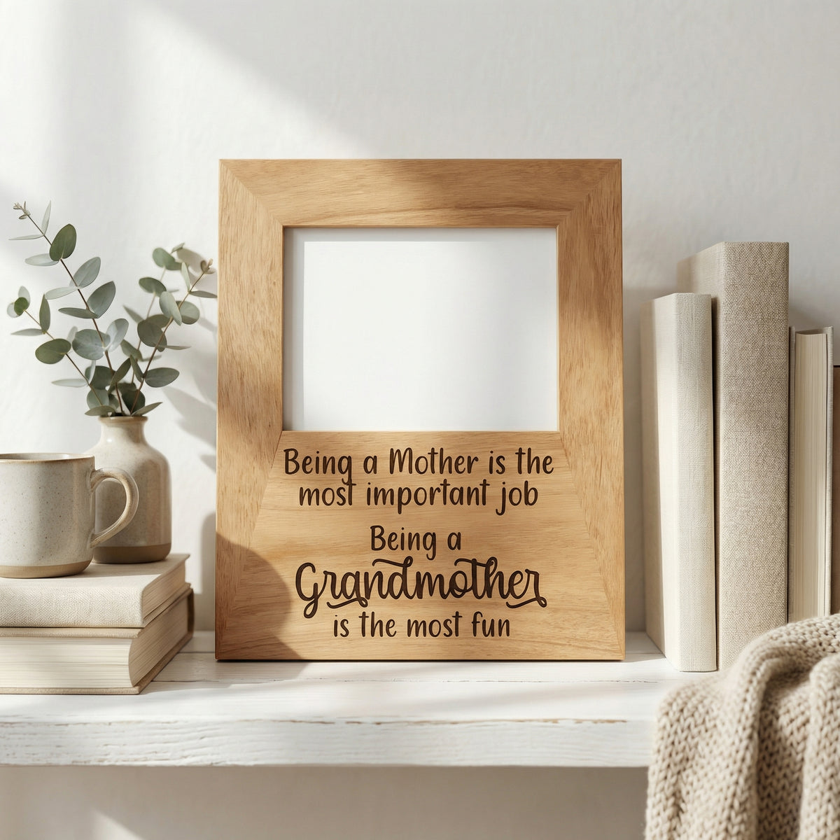 A wooden picture frame with a message about being a mother, placed on a shelf next to a stack of books and a plant.