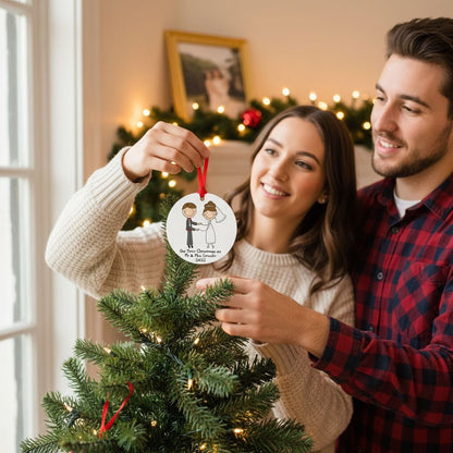 A man and a woman are decorating a Christmas tree together, with the woman holding a small ornament that features a couple.