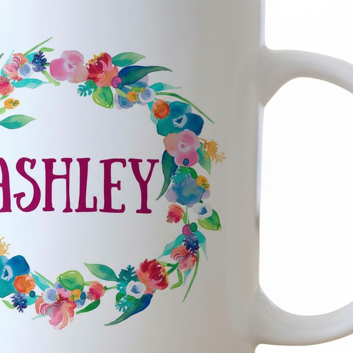 A white mug with a colorful floral wreath design and the name "Ashley" written on it.
