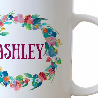 A white mug with a colorful floral wreath design and the name "Ashley" written on it.