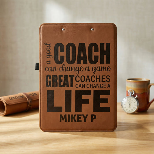 A brown clipboard with a motivational quote about coaches and their impact on lives, placed on a wooden surface with a rolled-up coaching mat and a coffee mug in the background.