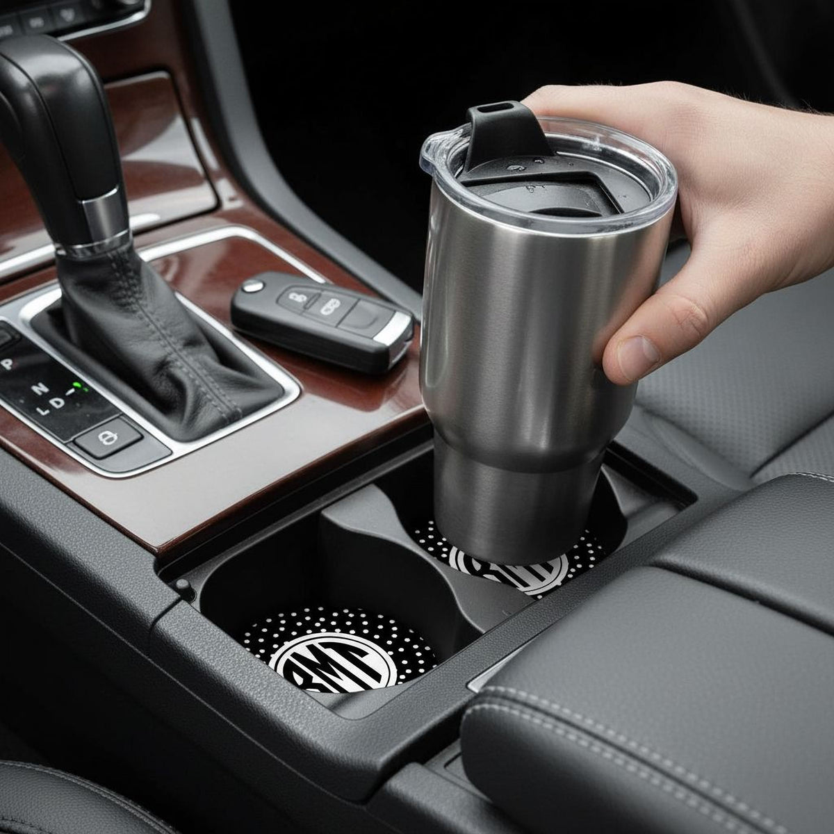 A person's hand is holding a stainless steel thermos in the car's cup holder.