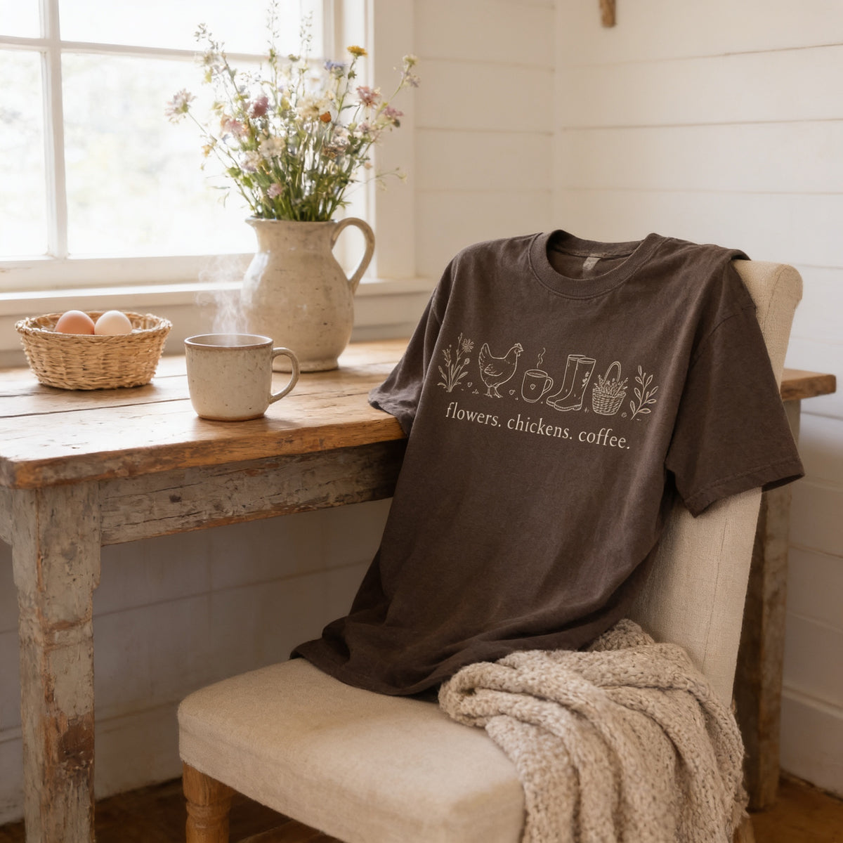 a cozy scene with a brown t-shirt hanging on a chair, a basket of eggs, a mug, and a vase of flowers on a wooden table.