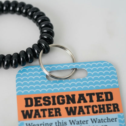 A black bead bracelet is shown next to a blue and white tag that reads "DESIGNATED WATER WATCHER" and "Wearing this Water Watcher".