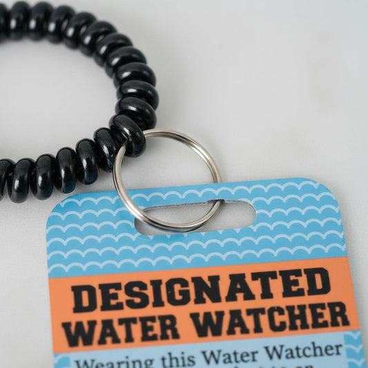 A black bead bracelet is shown next to a blue and white tag that reads "DESIGNATED WATER WATCHER" and "Wearing this Water Watcher".
