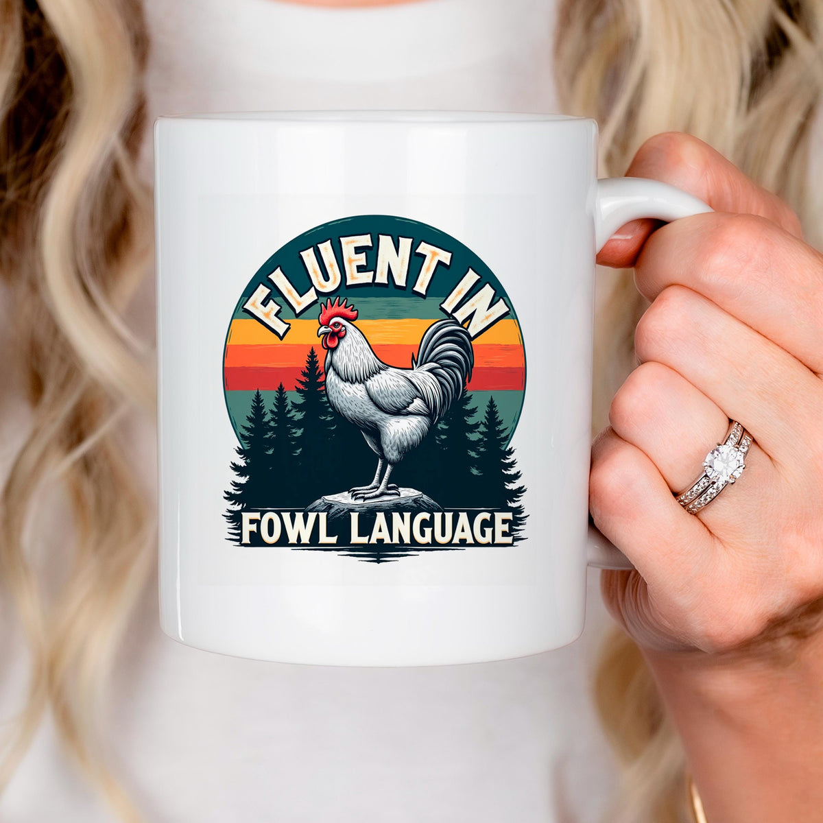 A person is holding a white mug with a graphic design featuring a rooster and the text "FLUENT IN FOWL LANGUAGE".
