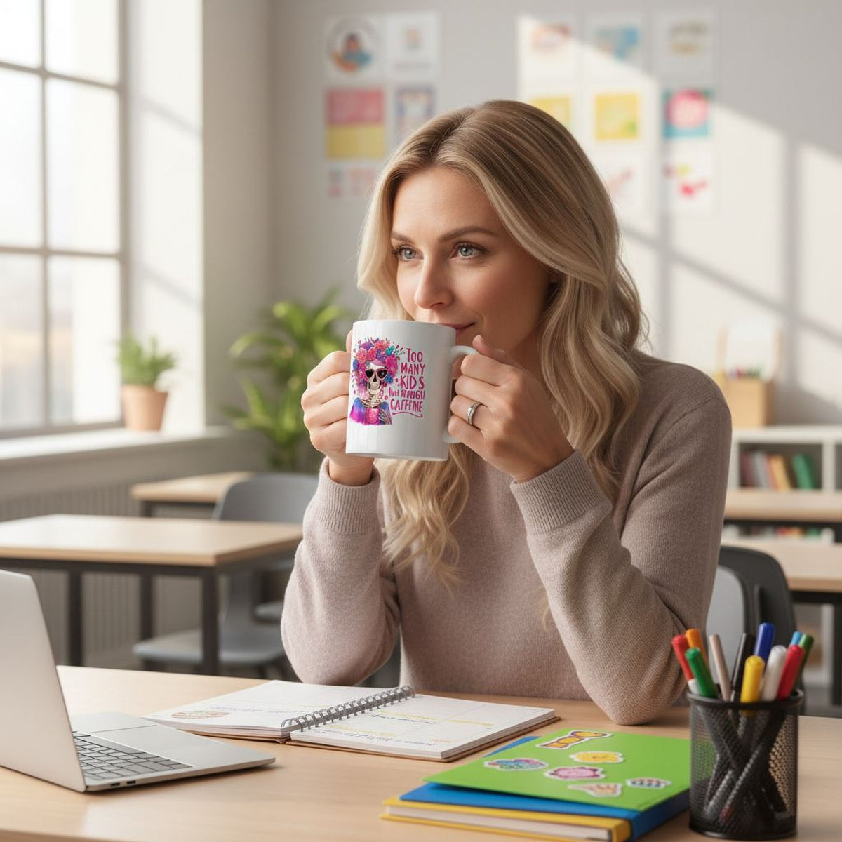 A woman with blonde hair is sitting at a desk, holding a mug and sipping a beverage. She is surrounded by various school supplies, including a laptop, notebook, and pencils.