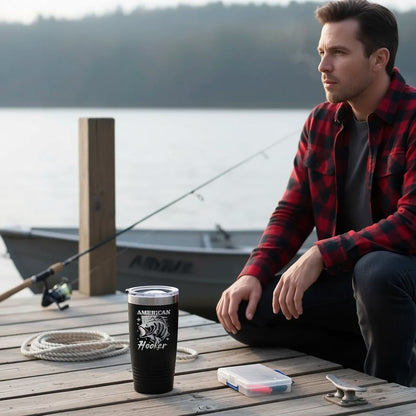 A man in a red and black plaid shirt sits on a wooden dock, holding a fishing rod and accompanied by a black tumbler with a lid and a rope.