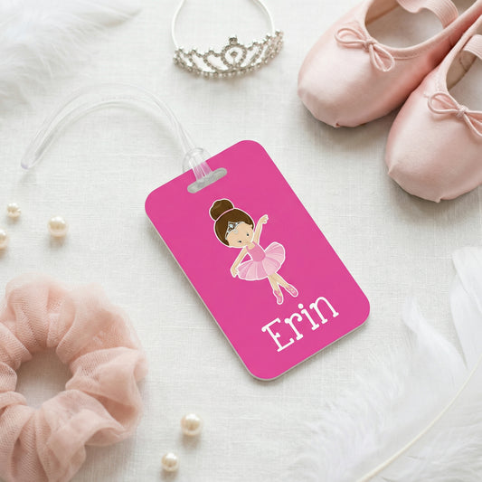 A pink name tag with a cartoon illustration of a young girl, surrounded by various accessories such as a tiara, ballet slippers, and pearls.