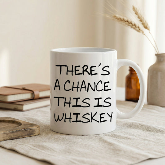 A white mug with black text that reads "THERE'S A CHANCE THIS IS WHISKEY" is placed on a table, with a stack of books and a vase of wheat stalks in the background.